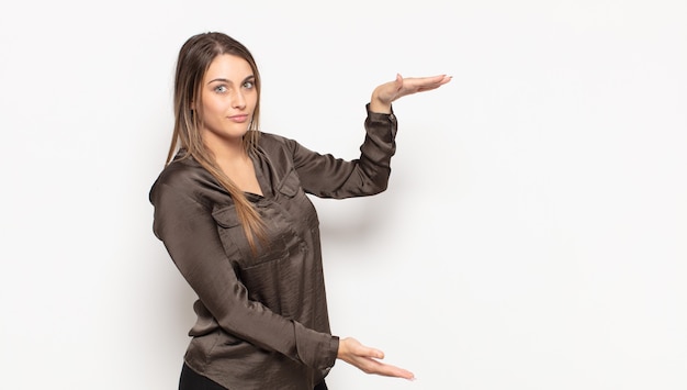 Young blonde woman holding an object with both hands on side copy space, showing, offering or advertising an object