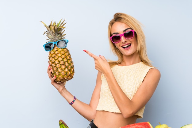 Giovane donna bionda in possesso di un ananas con occhiali da sole