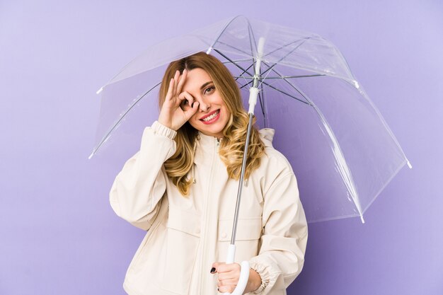 Young blonde woman holding an umbrella isolated Young blonde woman holding an umbrella isolated excited keeping ok gesture on eye.