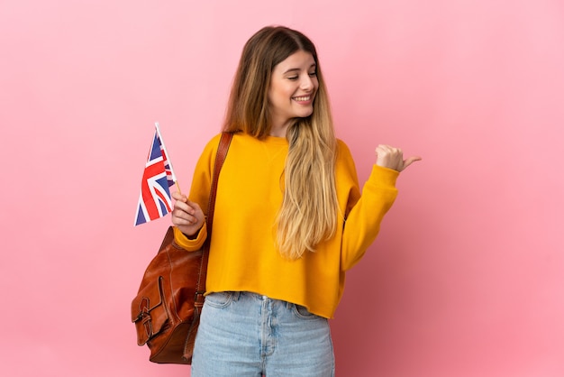製品を提示する側を指している白い壁に分離されたイギリスの旗を保持している若いブロンドの女性