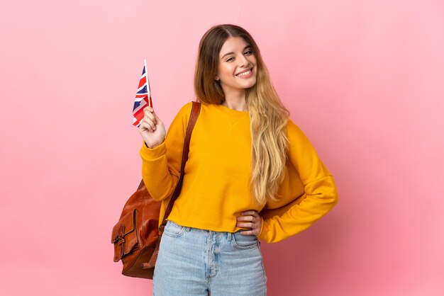 Young blonde woman holding an United Kingdom flag posing isolated against the blank wall