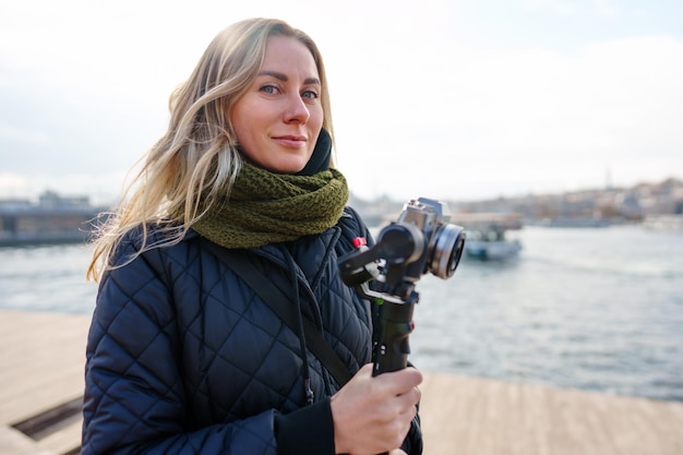 Young blonde woman holding video camera in hands while standing in the street of istanbul