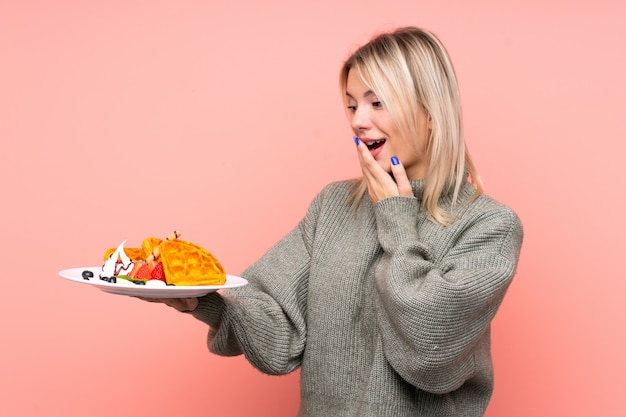 Foto la giovane donna bionda che tiene le cialde con la sorpresa e l'espressione facciale colpita