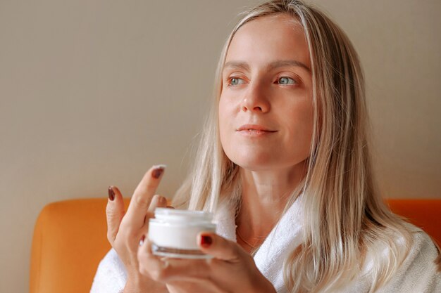 Foto una giovane donna bionda tiene una crema per il viso.