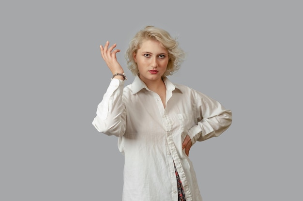 Фото Молодая блондинка в белой рубашке смотрит в камеру рука об руку, другая рука поднята вверх удивлен