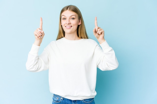 Young blonde woman indicates with both fore fingers up showing a blank space.