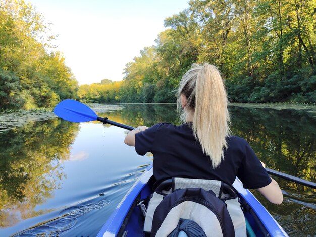 Молодая блондинка гребёт на байдарке на реке Задний вид Активный отдых и туризм