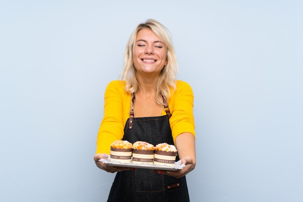 Young blonde woman over isolated background holding mini cakes