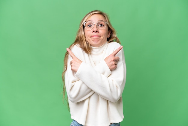 Young blonde woman over isolated background pointing to the laterals having doubts