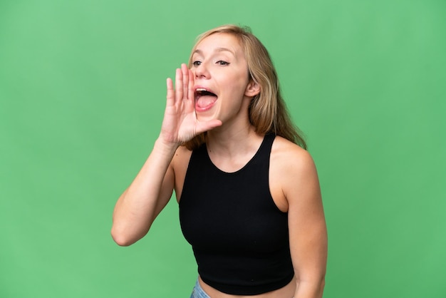 Young blonde woman over isolated background shouting with mouth wide open to the side