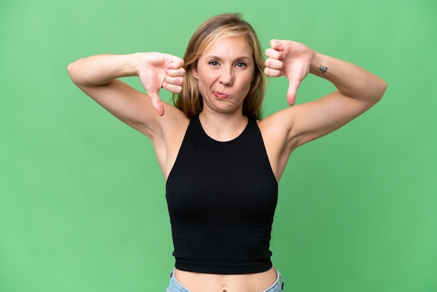 Young blonde woman over isolated background showing thumb down\
with two hands