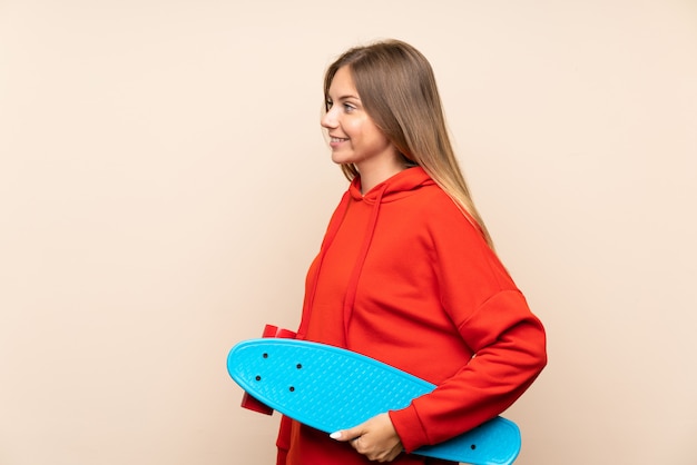 Young blonde woman over isolated background with skate