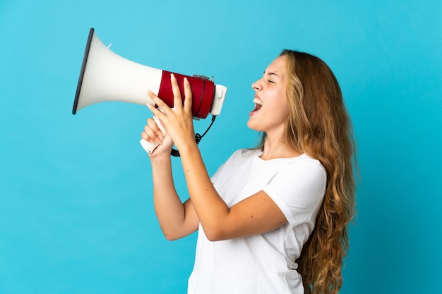 Young blonde woman isolated on blue background shouting through a megaphone