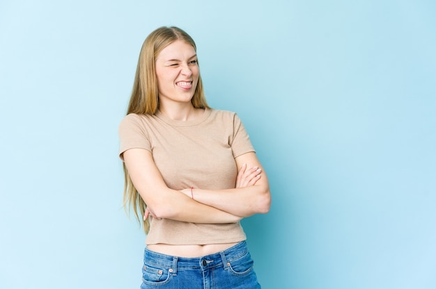 Young blonde woman isolated on blue wall funny and friendly sticking out tongue.