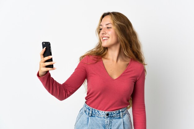 Young blonde woman isolated on blue wall making a selfie