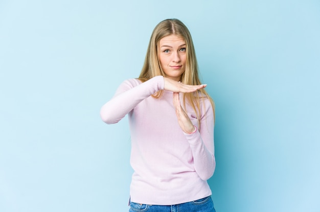 Giovane donna bionda isolata sulla parete blu che mostra un gesto di timeout.