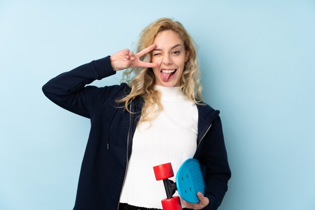 Young blonde woman isolated on blue wall with a skate with happy expression