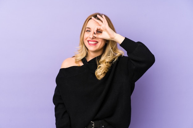 Young blonde woman isolated excited keeping ok gesture on eye.