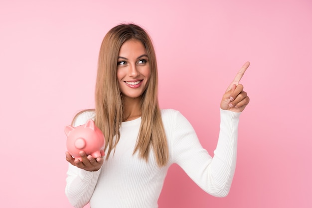 Young blonde woman over isolated  holding a big piggybank