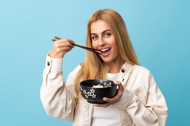 Young blonde woman isolated holding a bowl of noodles with chopsticks