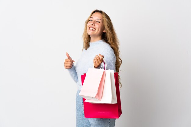 Young blonde woman isolated holding shopping bags and with thumb up