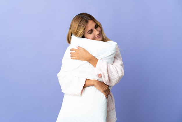 Young blonde woman isolated in pajamas and holding a pillow while sleeping