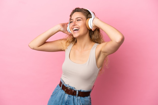 Young blonde woman isolated on pink background listening music