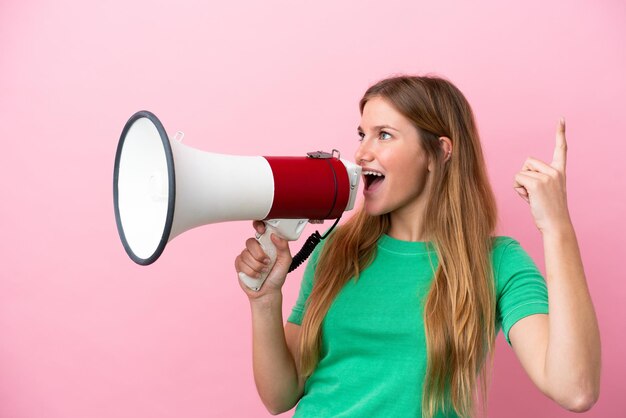 Photo young blonde woman isolated on pink background shouting through a megaphone to announce something in lateral position