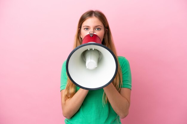 Young blonde woman isolated on pink background shouting through a megaphone to announce something