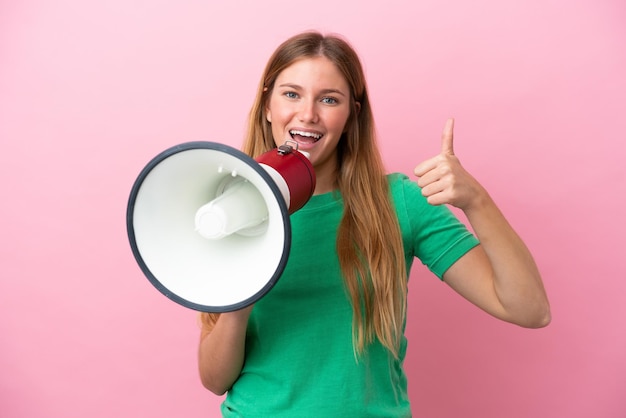 Young blonde woman isolated on pink background shouting through a megaphone and pointing side