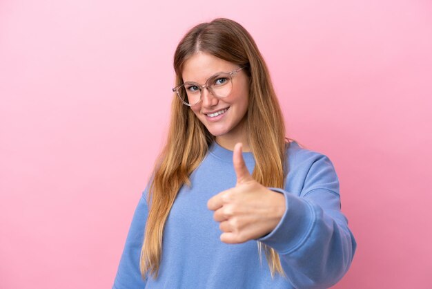 Young blonde woman isolated on pink background With glasses and with thumb up