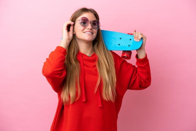 Young blonde woman isolated on pink background with a skate and looking up