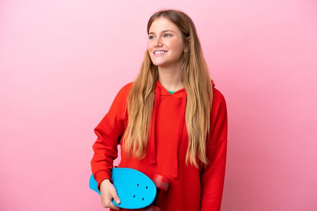 Young blonde woman isolated on pink background with a skate