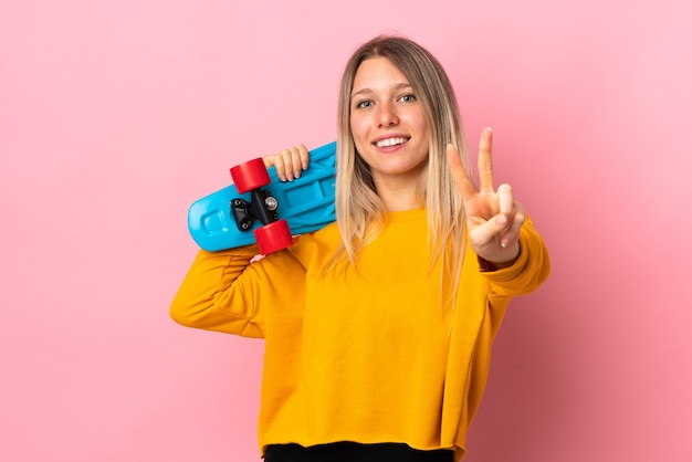 Young blonde woman isolated on pink wall with a skate doing victory gesture