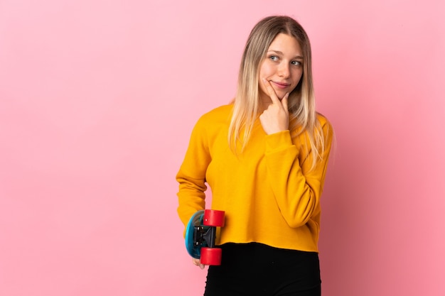 Giovane donna bionda isolata sulla parete rosa con un pattino e guardando laterale