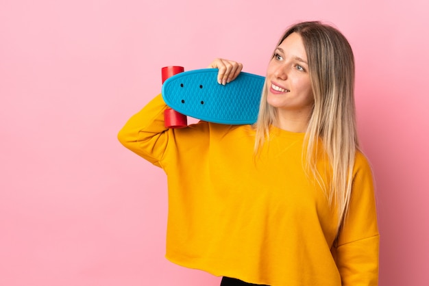 Giovane donna bionda isolata sulla parete rosa con un pattino