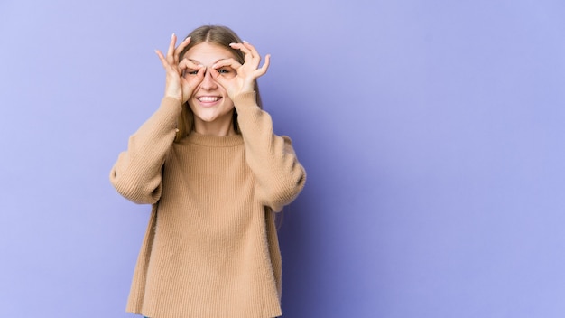 Young blonde woman isolated on purple background excited keeping ok gesture on eye.