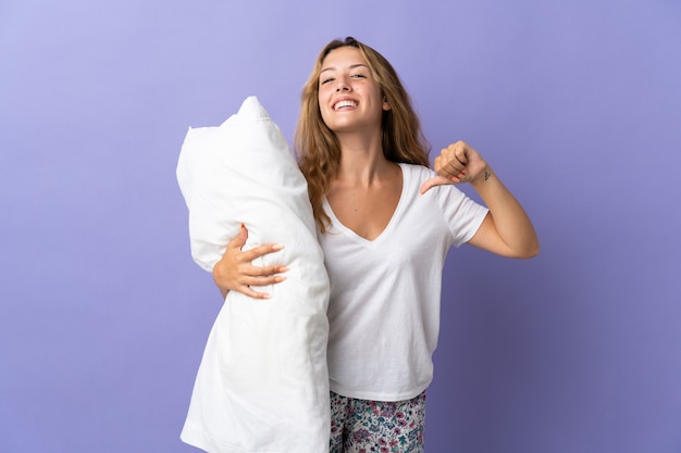 Young blonde woman isolated on purple in pajamas and proud of self-satisfied