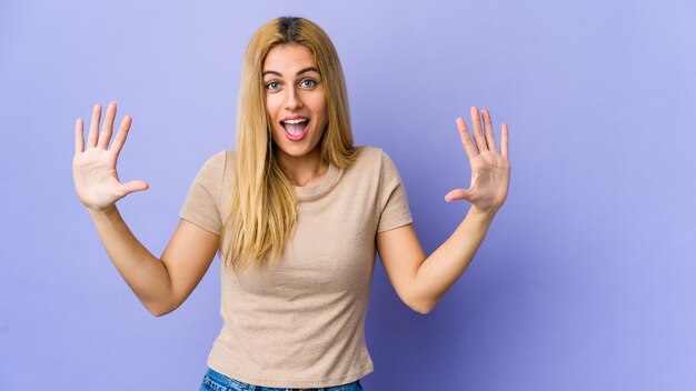 Young blonde woman isolated on purple receiving a pleasant surprise, excited and raising hands.