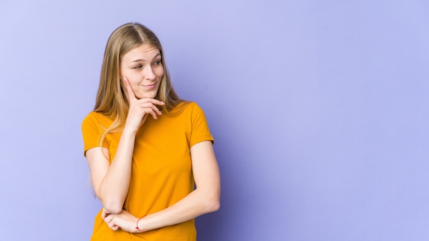 Young blonde woman isolated on purple wall contemplating, planning a strategy, thinking about the way of a business