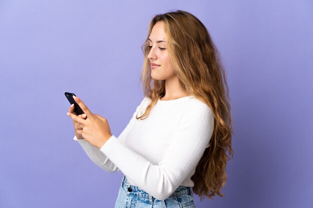 Young blonde woman isolated sending a message or email with the mobile