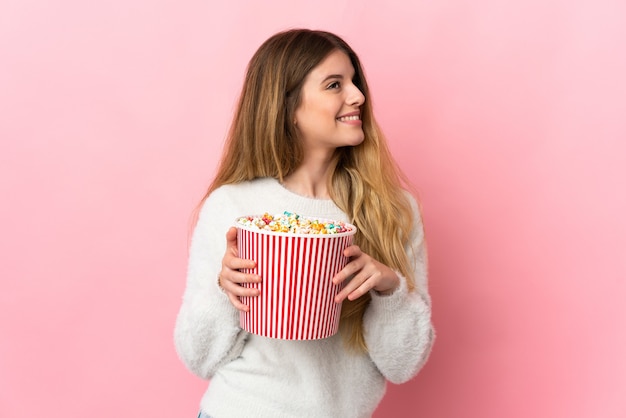 Young blonde woman over isolated wall holding a big bucket of popcorns