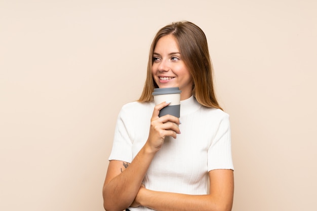 Young blonde woman over isolated wall holding coffee to take away