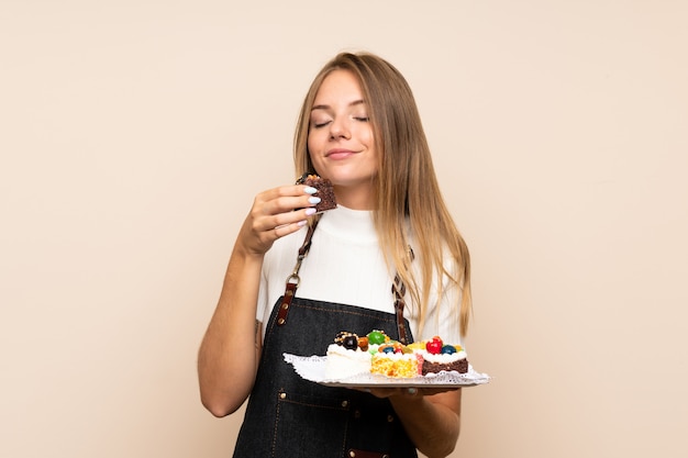 Young blonde woman over isolated wall holding mini cakes