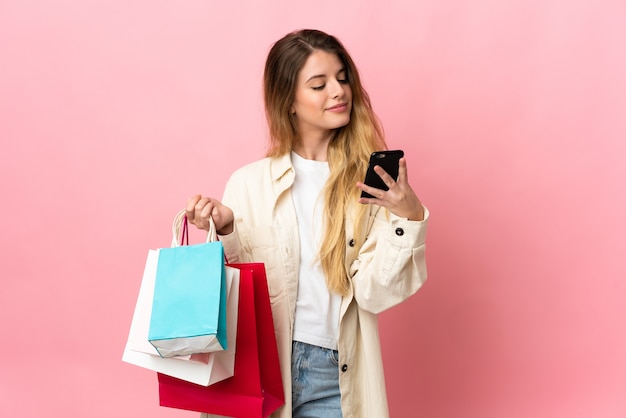 쇼핑 가방을 들고 친구에게 그녀의 휴대 전화로 메시지를 작성하는 고립 된 벽 위에 젊은 금발의 여자