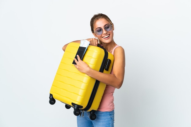 Young blonde woman over isolated wall in vacation with suitcase and passport