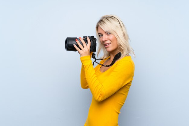 Young blonde woman over isolated wall with a professional camera