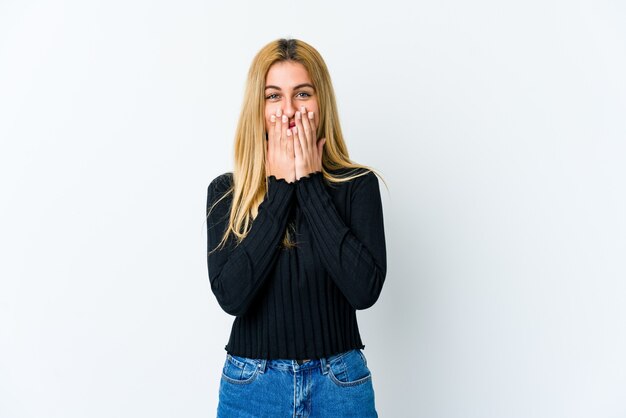 Young blonde woman isolated on white laughing about something, covering mouth with hands.