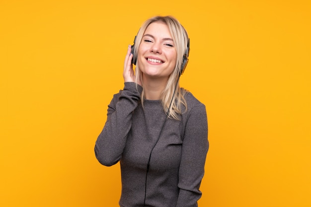 Young blonde woman over isolated yellow wall listening music