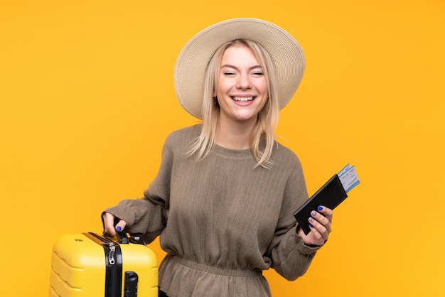 Young blonde woman over isolated yellow wall in vacation with suitcase and passport